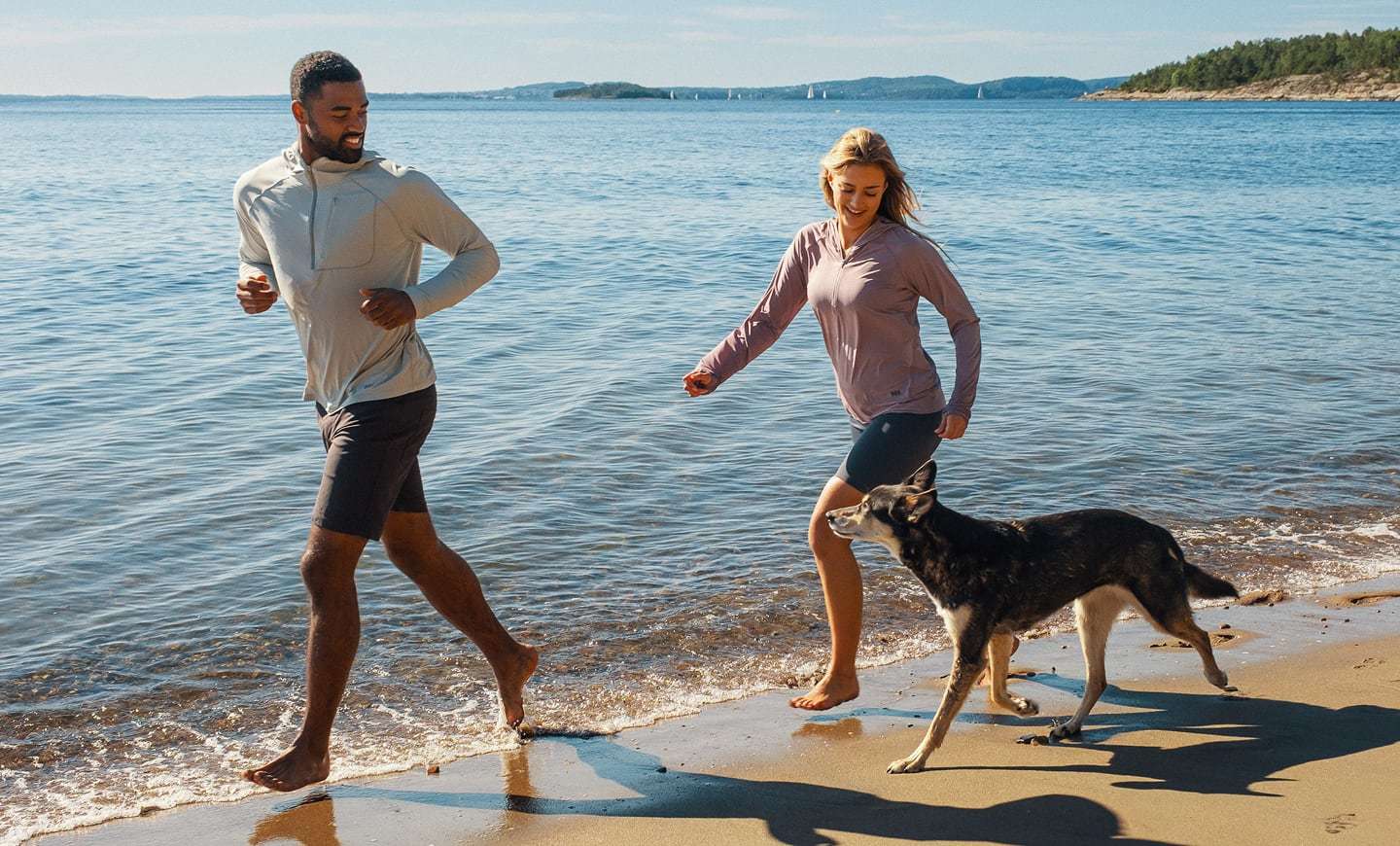 Man and woman with dog on the beach, wearing Helly Hansen sun protective clothing
