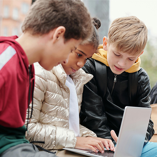 Tre bambini si sono concentrati sullo schermo di un laptop all'aperto.