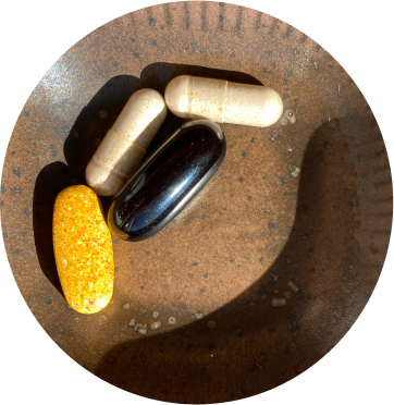 alt="Primo piano di capsule e softgel di integratori alimentari assortiti su un piatto di ceramica marrone, illuminato dalla luce solare naturale.»