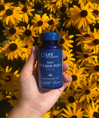 alt="Tenere in mano un flacone di integratore di acido Super R-Lipoico Life Extension su uno sfondo di fiori giallo brillante.»