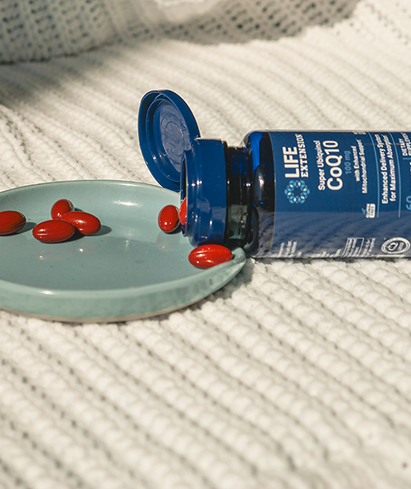 alt="Flacone aperto di Life Extension Super Ubiquinol CoQ10 softgels stese su una superficie ruvida, con capsule rosse sparse su una piccola piastra blu chiaro.»