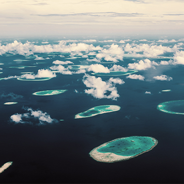 An aerial view of small islands surrounded by the deep blue ocean and white clouds.