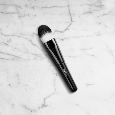 Un elegante pennello da trucco nero con una punta di setole bianche, appoggiato su uno sfondo di marmo bianco.