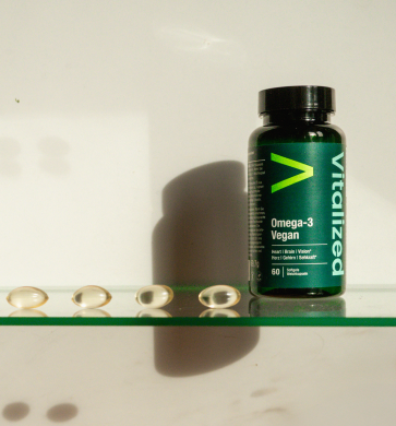 alt="Bottiglia vegana vitalizzata di Omega-3 con capsule disposte in fila su un ripiano di vetro»