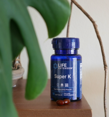 alt="Flacone Life Extension Super K con softgel su una mensola di legno accanto a una pianta verde»