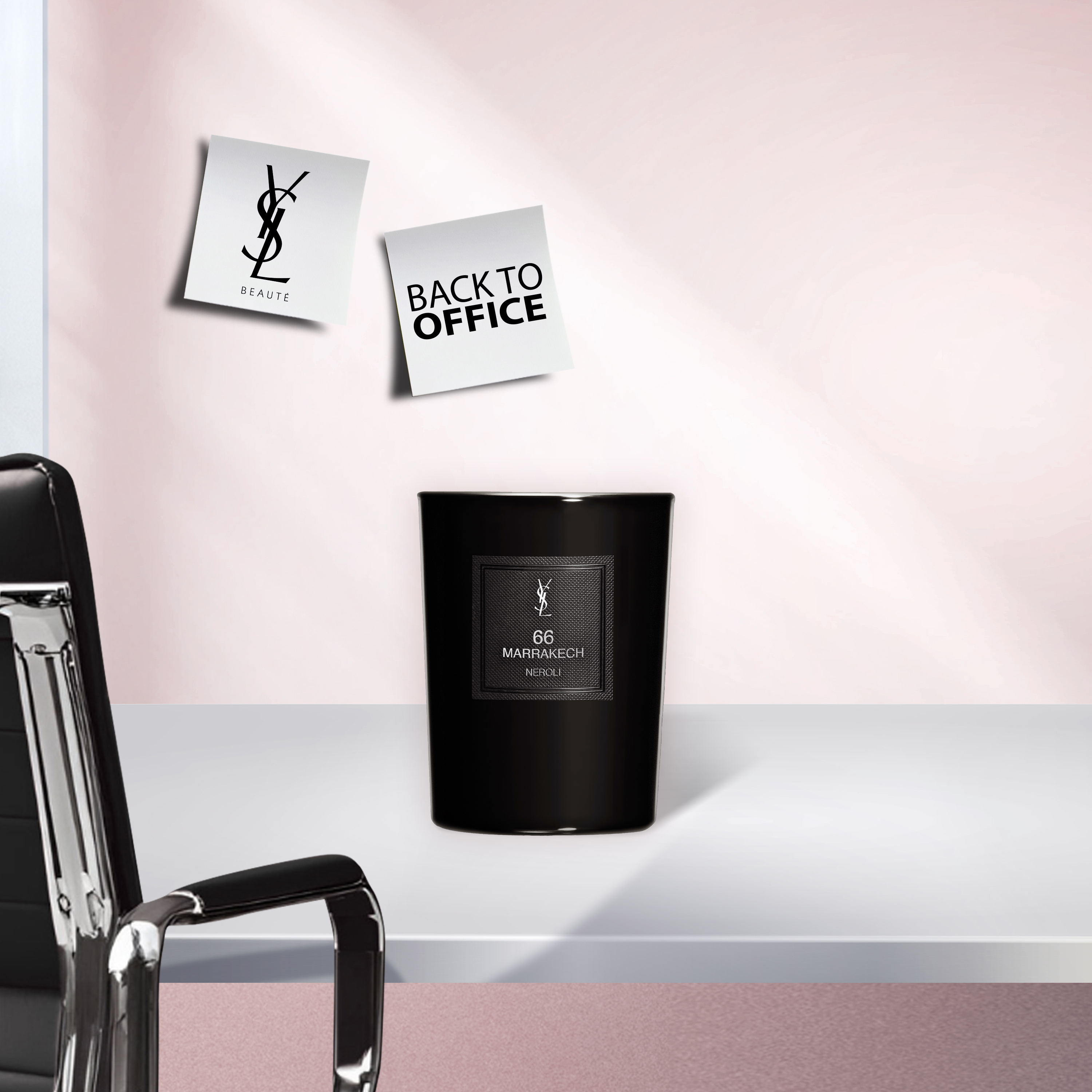 Una candela nera YSL "66 Marrakech Neroli" su una scrivania bianca in un ambiente d'ufficio, con una sedia da ufficio nera a sinistra e due post-it "YSL BEAUTÉ" e "BACK TO OFFICE" su una parete rosa chiaro.
