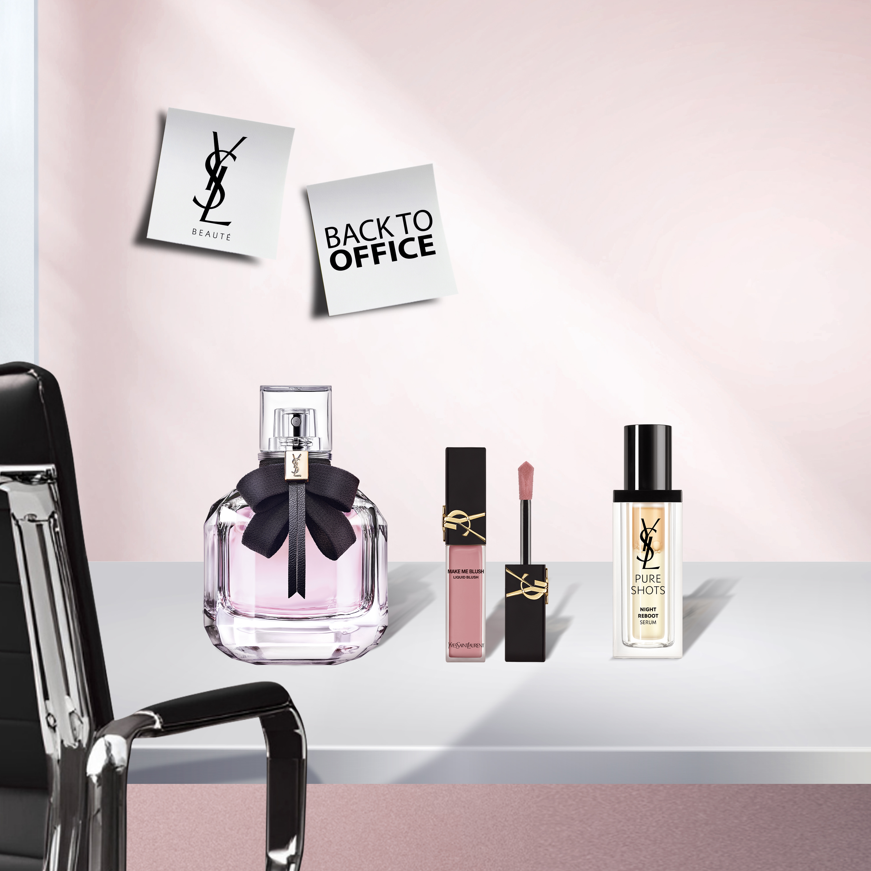 Una scena d'ufficio con un profumo YSL Mon Paris (flacone rosa con fiocco nero), un lucidalabbra YSL "Make Me Blush" e un siero YSL Pure Shots Night Reboot su una scrivania bianca. Una sedia da ufficio nera è visibile a sinistra, e due post-it "YSL BEAUTÉ" e "BACK TO OFFICE" sono appuntati sul muro rosa chiaro.