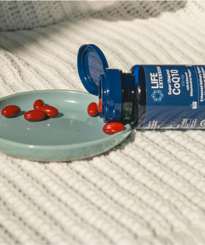 alt="Bottle of Life Extension Super Ubiquinol CoQ10 versando capsule softgel rosse su un piccolo piatto su una superficie ruvida»