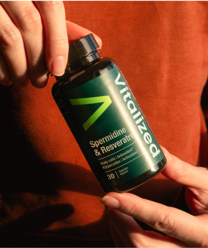 alt="Mani che tengono in mano un flacone di integratore alimentare di spermidina vitalizzata e resveratrolo con un'etichetta verde scuro»