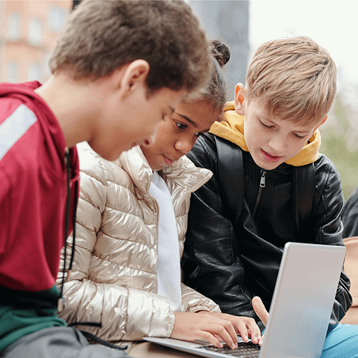 Tre bambini si sono concentrati sullo schermo di un laptop all'aperto.