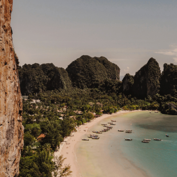 A scenic beach in Phuket with clear water, boats along the shore, and green hills in the background.
