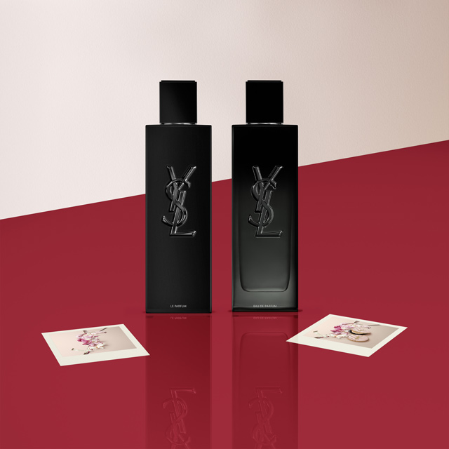 Due profumi Yves Saint Laurent (YSL) Y di diverse dimensioni, nelle loro bottiglie nere, esposti su una superficie rossa con piccole carte logo YSL.