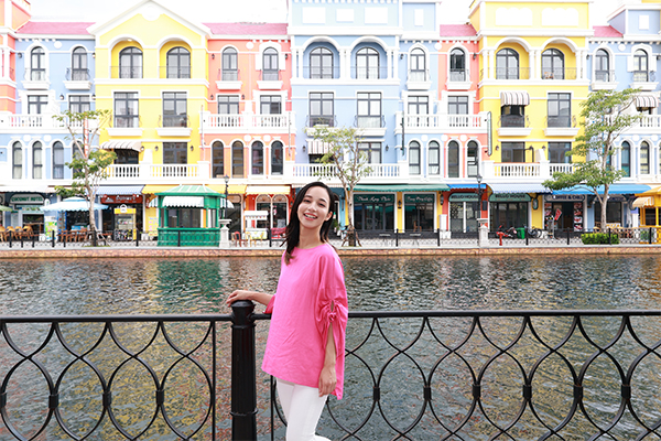 Una persona sorridente con una camicia rosa davanti a edifici colorati e a un canale.