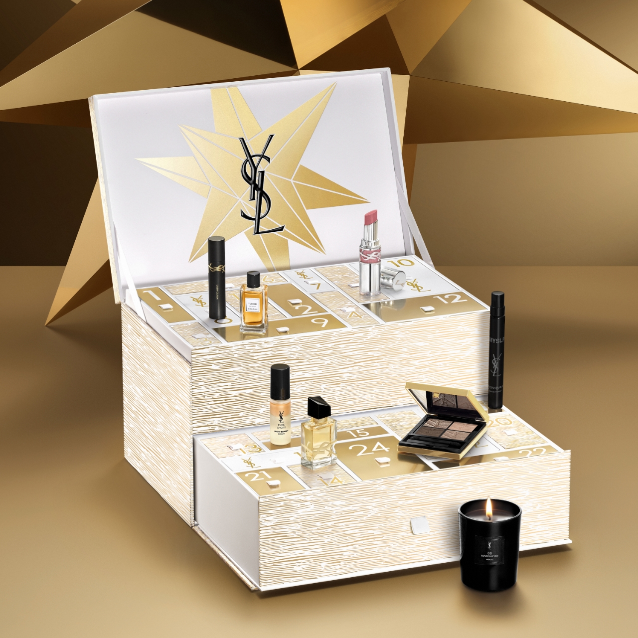 Calendario dell'Avvento di lusso Yves Saint Laurent (YSL) aperto, che rivela vari prodotti di bellezza tra cui mascara, profumi, rossetto, smalto per unghie, una palette di ombretti e una candela accesa, all'interno di scomparti numerati. L'interno del coperchio presenta il logo YSL e disegni a stella, il tutto su uno sfondo geometrico dorato