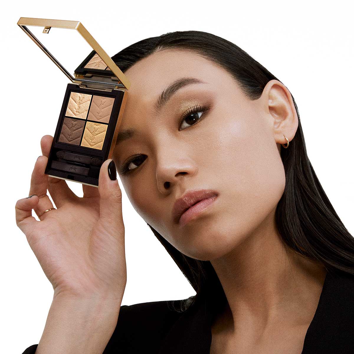 Una donna dai capelli scuri e trucco delicato tiene in mano una palette di ombretti Yves Saint Laurent aperta con quattro tonalità calde, guardando direttamente la fotocamera.