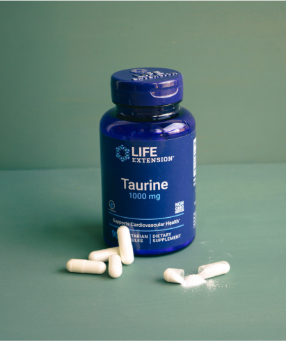 alt="Life Extension Taurine Flacone da 1000 mg con diverse capsule bianche e polvere versata su una superficie verde.»