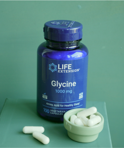 alt="Bottle of Life Extension Glycine 1000 mg con capsule bianche in una piccola ciotola, su sfondo verde.»