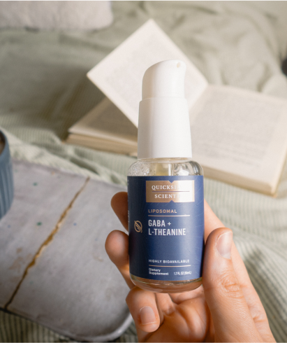 alt="Flacone spray liposomiale Quicksilver Scientific GABA + L-teanina tenuto in mano, con un libro aperto e un'accogliente ambientazione sullo sfondo.»