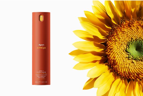 Balsamo spray senza risciacquo Dyson Omega accanto a un girasole.