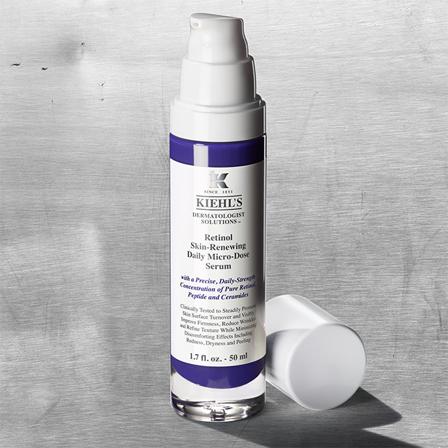 Flacone bianco e viola del Kiehl’s Retinol Skin-Renewing Daily Micro-Dose Serum, con tappo bianco aperto su sfondo grigio metallico.