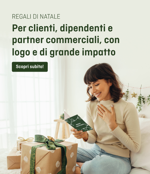 Una persona è seduta su un divano e tiene in mano un biglietto con un motivo verde e bianco, accanto a lei ci sono dei regali con un nastro verde su uno sfondo chiaro.