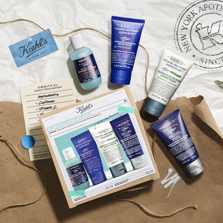 Set The Grooming Collection Kiehl’s disposto su carta kraft con i quattro prodotti: detergente, crema da barba, dopobarba e idratante. Accanto, scheda con ingredienti e cartoncino con logo Kiehl’s.