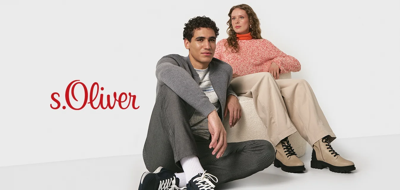 Due giovani adulti in abbigliamento casual autunnale; uno seduto sul pavimento in sneakers, l'altro su una sedia bassa con stivali beige, su uno sfondo bianco.