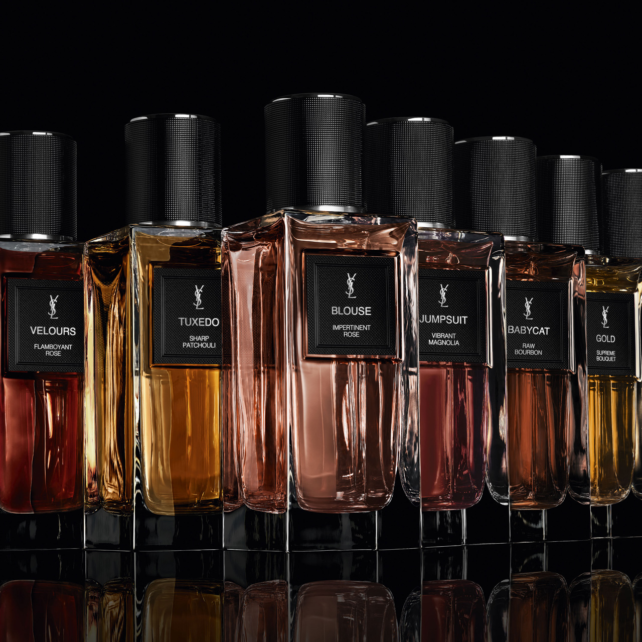 Una fila perfettamente allineata di diverse bottiglie di profumo YSL, ciascuna con un tappo nero e un'etichetta distintiva (ad esempio, "VELOURS", "TUXEDO", "BLOUSE", "JUMPSUIT", "BABYCAT", "GOLD"), si trova su una superficie nera riflettente contro uno sfondo scuro, mostrando le loro varie tonalità ambrate e rossastre.