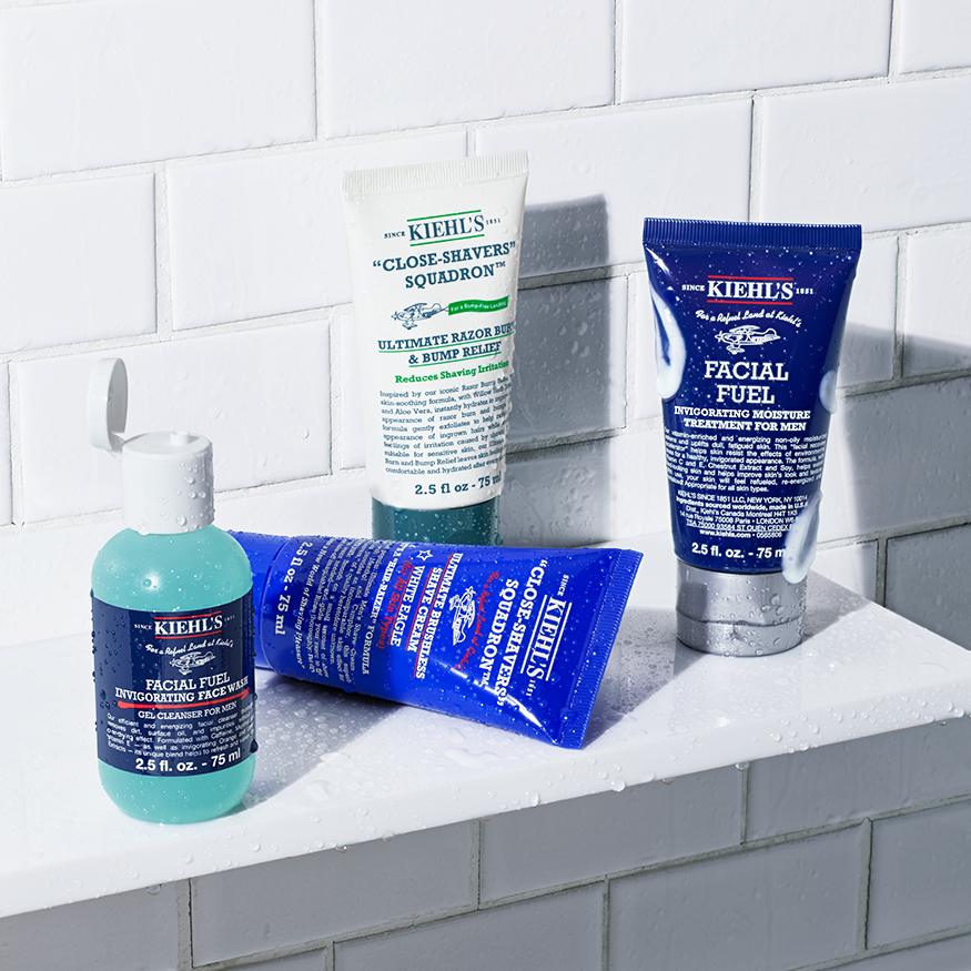 Prodotti del set The Grooming Collection Kiehl’s su mensola di piastrelle bianche, coperti da gocce d’acqua che richiamano l’ambiente doccia.