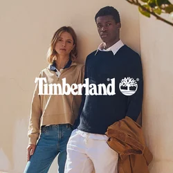 Due persone stanno su un terrazzo di pietra accanto a un muro giallo con persiane verdi, indossando abiti casual dai colori tenui.