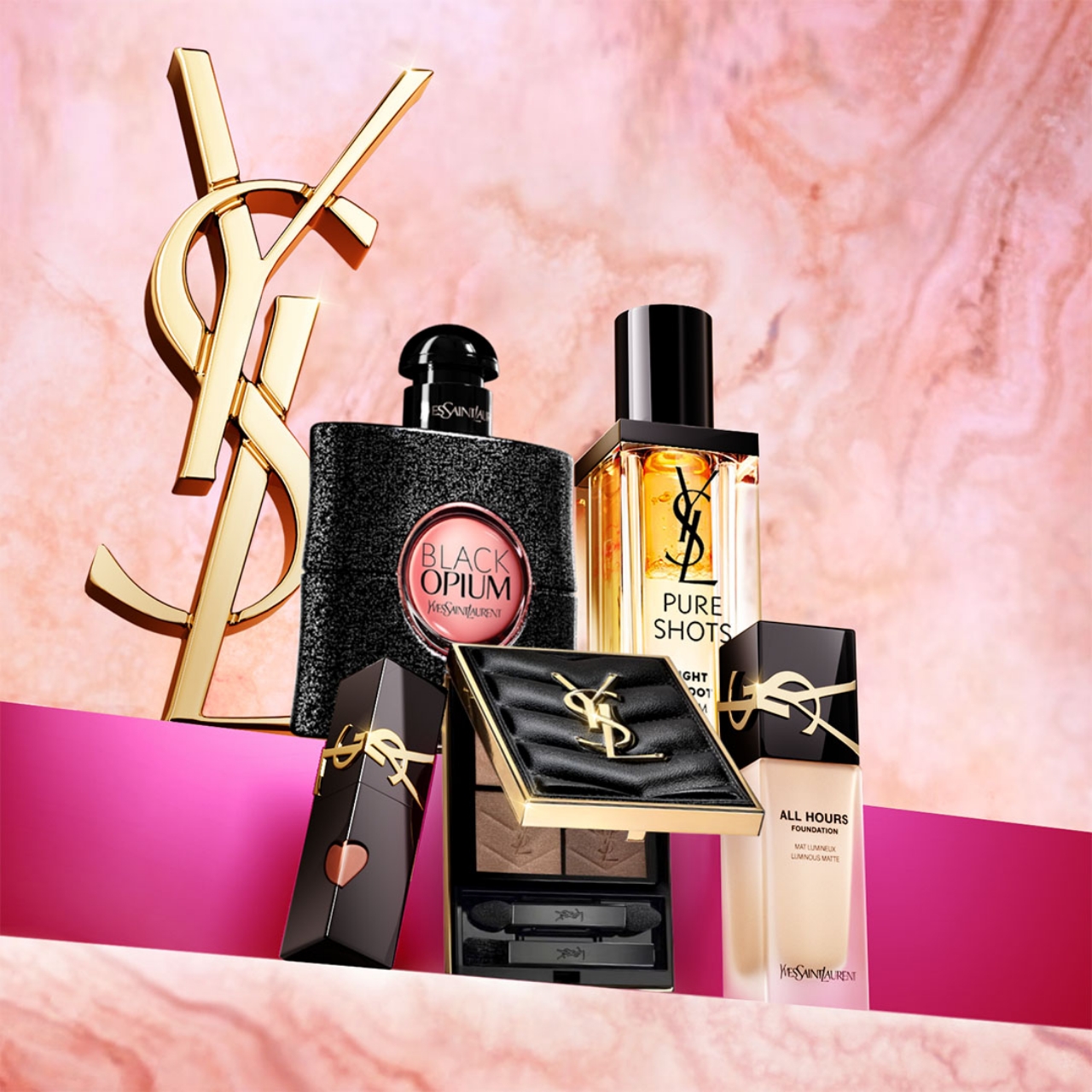 Una collezione di prodotti di bellezza Yves Saint Laurent, tra cui i profumi Black Opium e Pure Shots, una palette di ombretti, un rossetto e il fondotinta All Hours Foundation, esposti con un grande logo YSL dorato su uno sfondo rosa