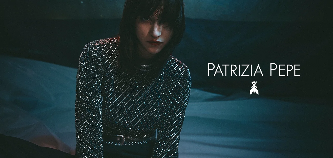 Maglietta a maniche lunghe nera e argento con un motivo a griglia, dotata di paillettes e una cintura metallica, su uno sfondo scuro e strutturato.