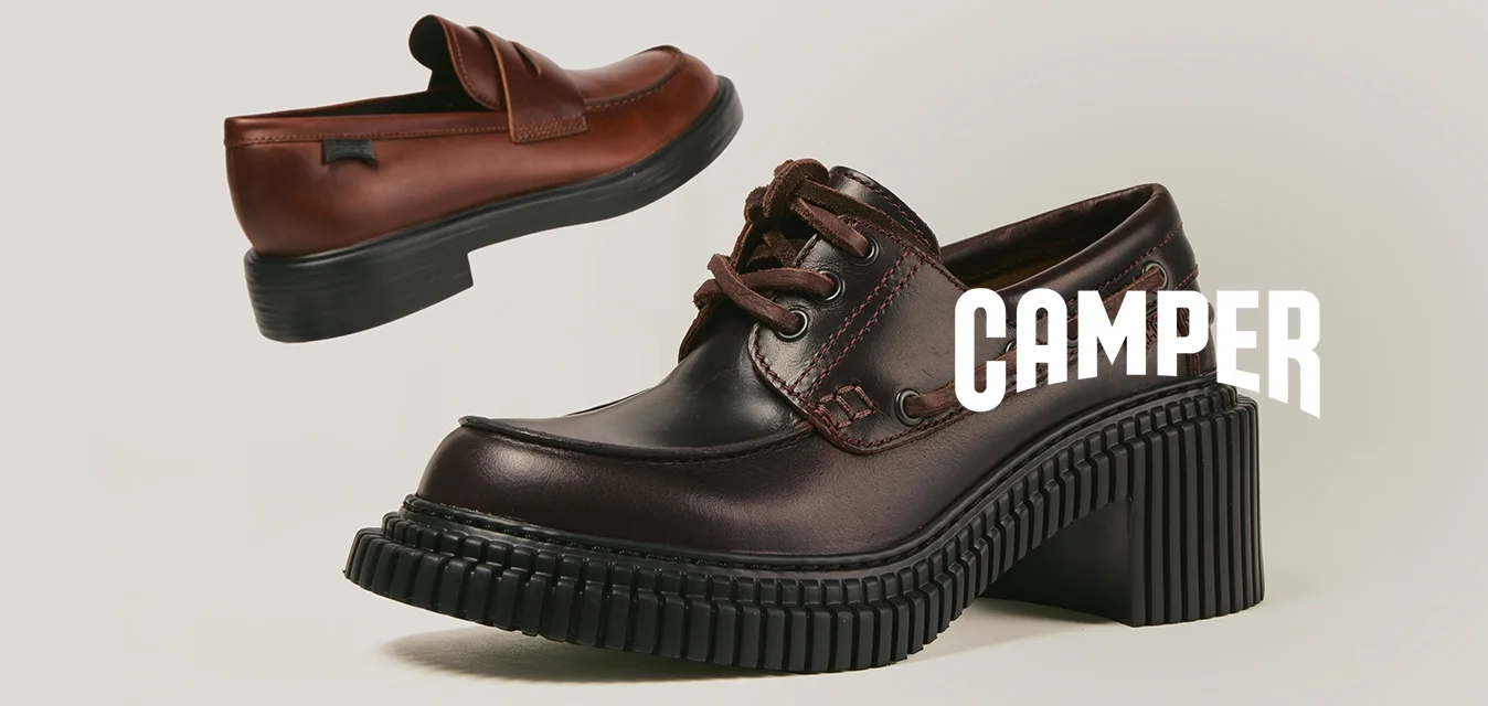 Due scarpe di pelle marrone con suole nere spesse, una mocassino e una stringata, esposte su uno sfondo beige semplice.