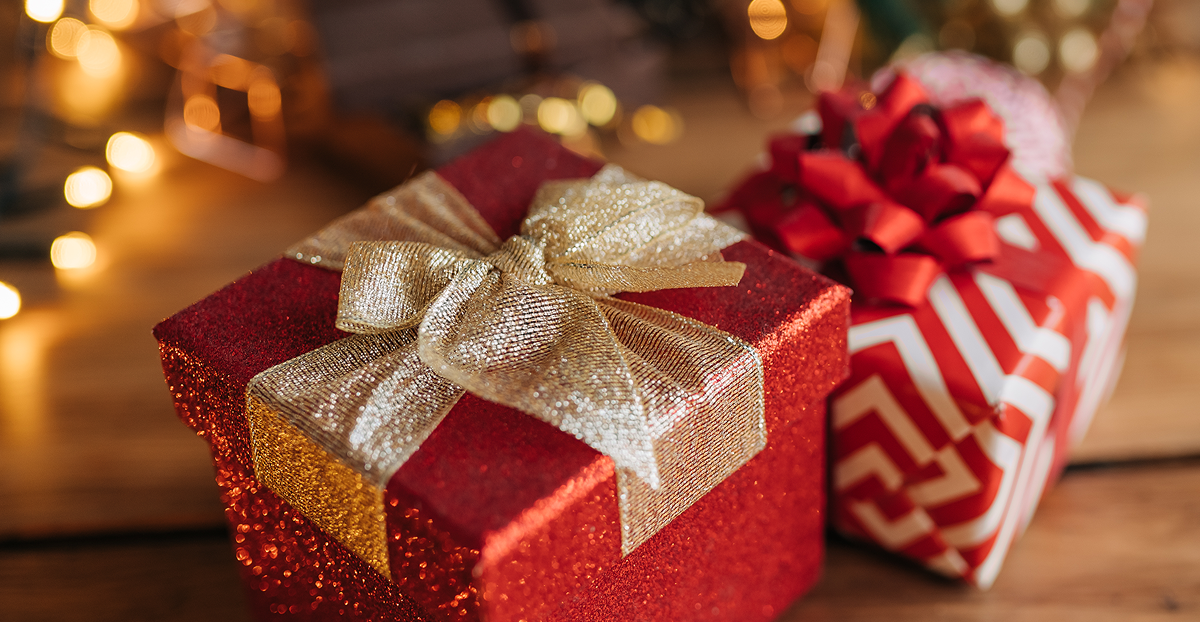Una confezione regalo rossa scintillante con un fiocco dorato accanto a un regalo con motivi rossi e bianchi, circondata da calde luci bokeh.