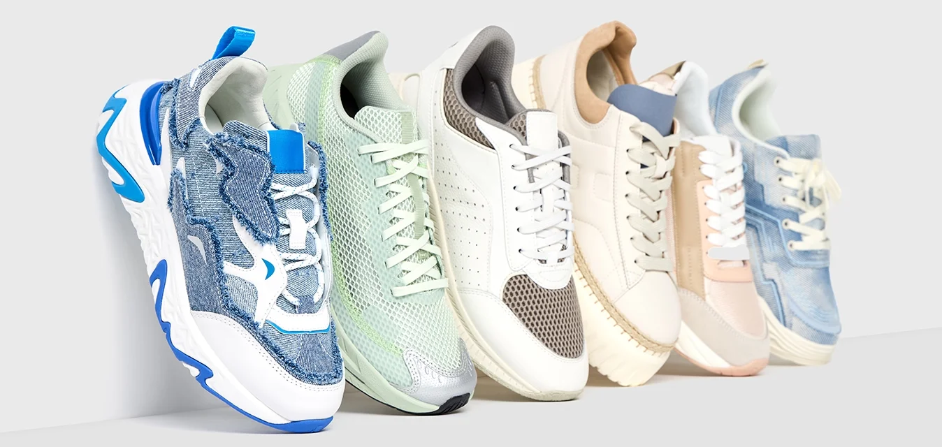Cinque paia di sneakers: in rete blu e bianca, in rete verde menta, in pelle perforata grigia, in pelle crema e in denim azzurro chiaro, con design e texture variabili.