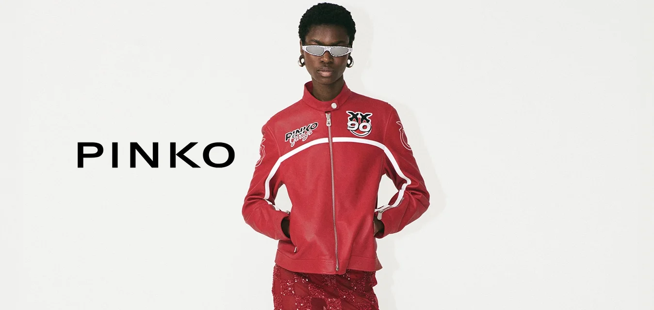 Giacca rossa con zip e dettagli con logo, abbinata a una gonna midi rossa in pizzo con motivo a scacchi e sandali bianchi con tacco.