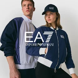 Due giovani adulti in posa con giacche zip-up navy e bianche, uno dei quali indossa un cappellino navy, su uno sfondo chiaro e semplice.