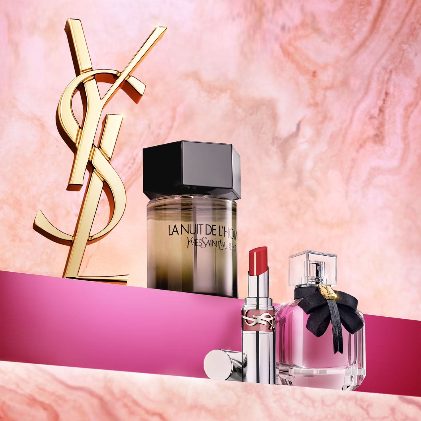 Una collezione di prodotti Yves Saint Laurent, tra cui i profumi La Nuit de l'Homme e Mon Paris, un rossetto e un mascara, disposti con un grande logo YSL dorato su uno sfondo rosa e marmorizzato.
