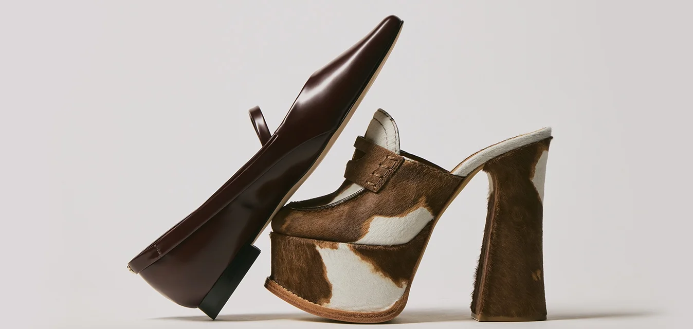 Scarpa mocassino in pelle marrone appoggiata contro un mule in pelle di mucca marrone e bianca con tacco alto a blocco su uno sfondo bianco.