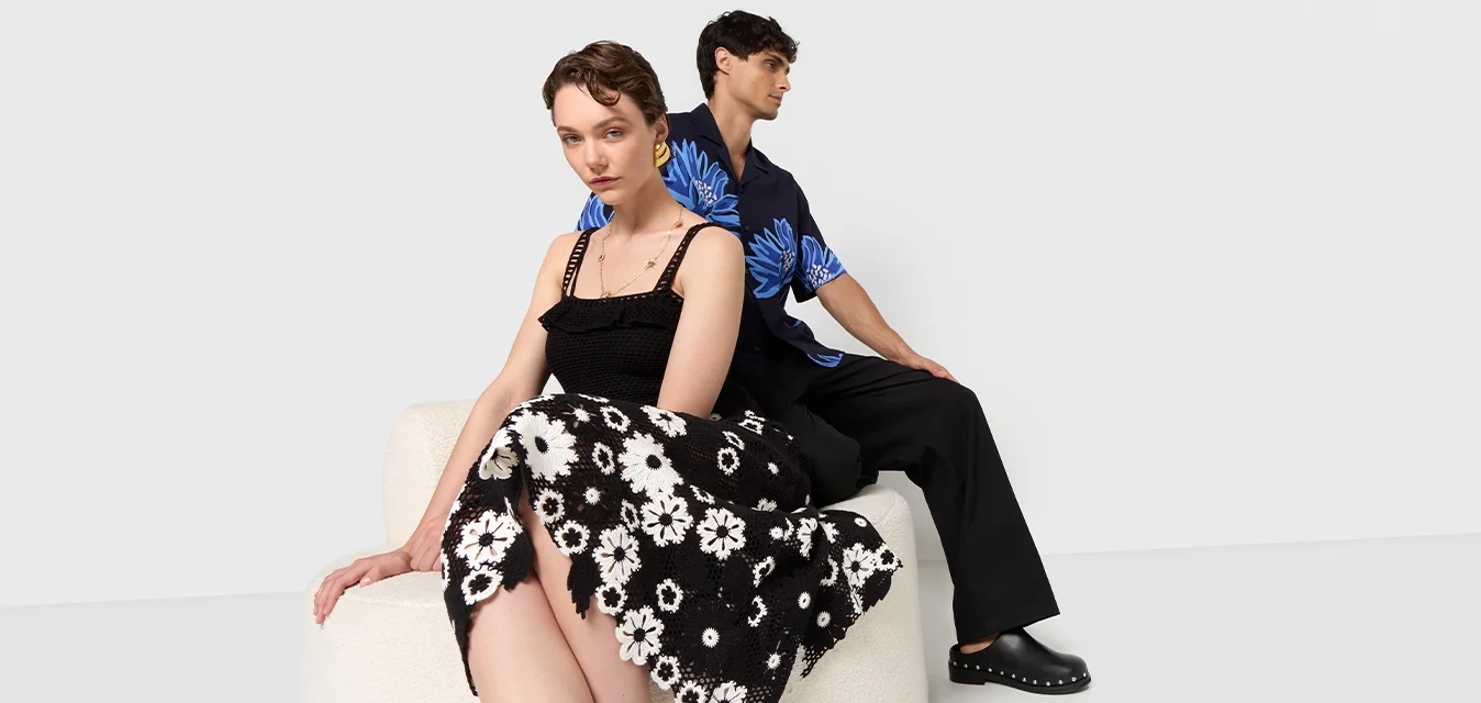 Gonna floreale in bianco e nero, top nero a trama, camicia floreale blu e pantaloni neri. Superfici lisce e motivi a contrasto presenti.