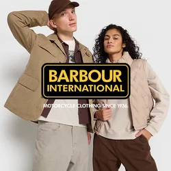 Uomo in giacca beige e cappellino con la mano dietro la testa, donna in gilet beige e felpa con la mano in tasca, entrambi in piedi su uno sfondo bianco.