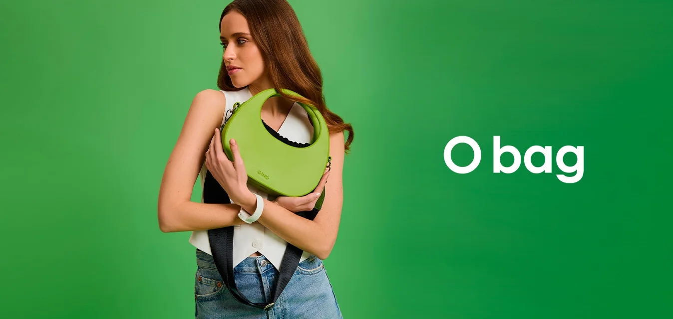 Borsa a mano verde curve realizzata in materiale morbido con una maniglia unica, accentuata da un interno nero a contrasto. Indossata con una tracolla nera.