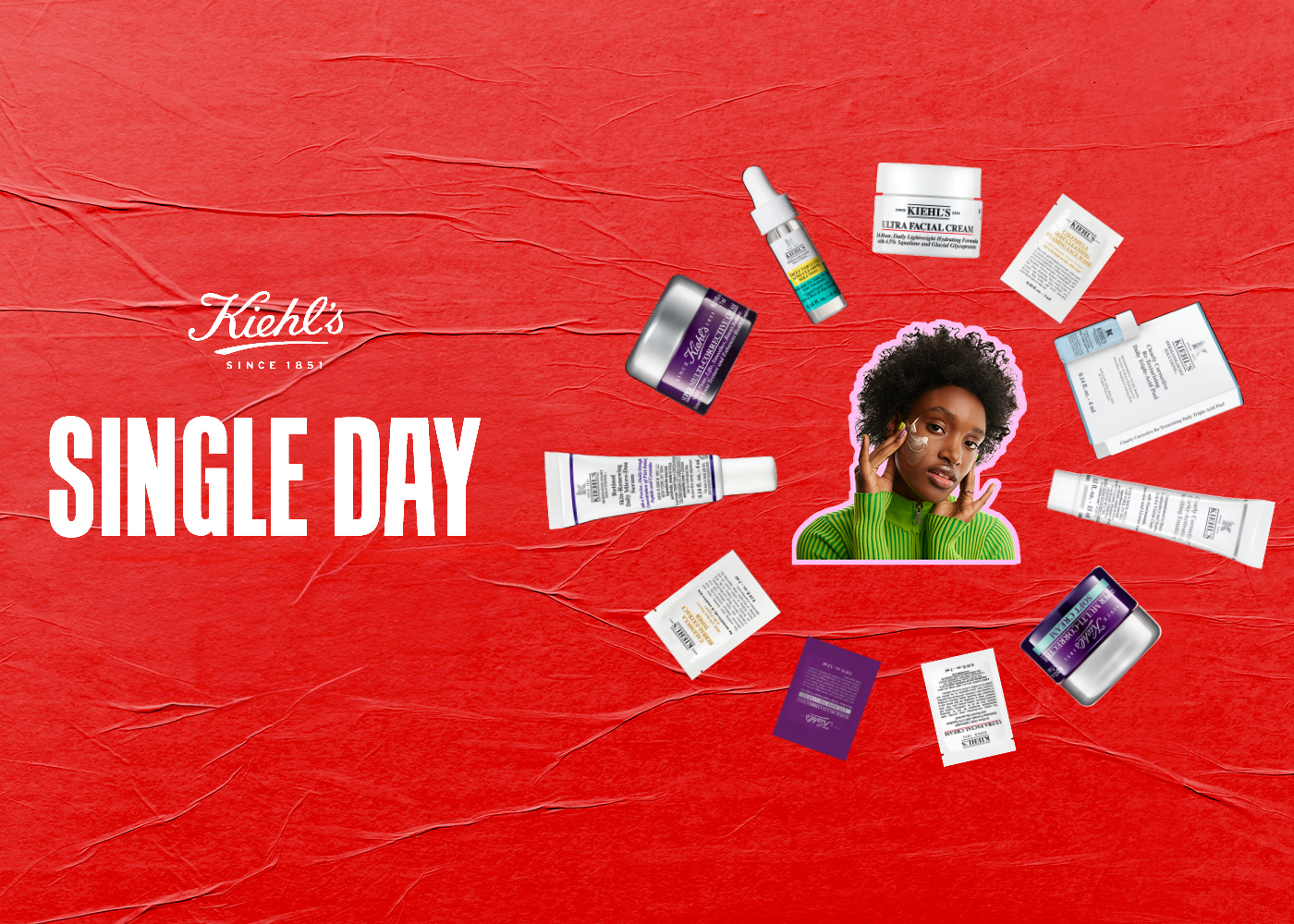 Visual Kiehl’s Single Days con sfondo rosso testurizzato. Al centro una persona con maglione verde applica crema viso, circondata da prodotti skincare Kiehl’s e campioni disposti in cerchio attorno al testo “Single Days”.