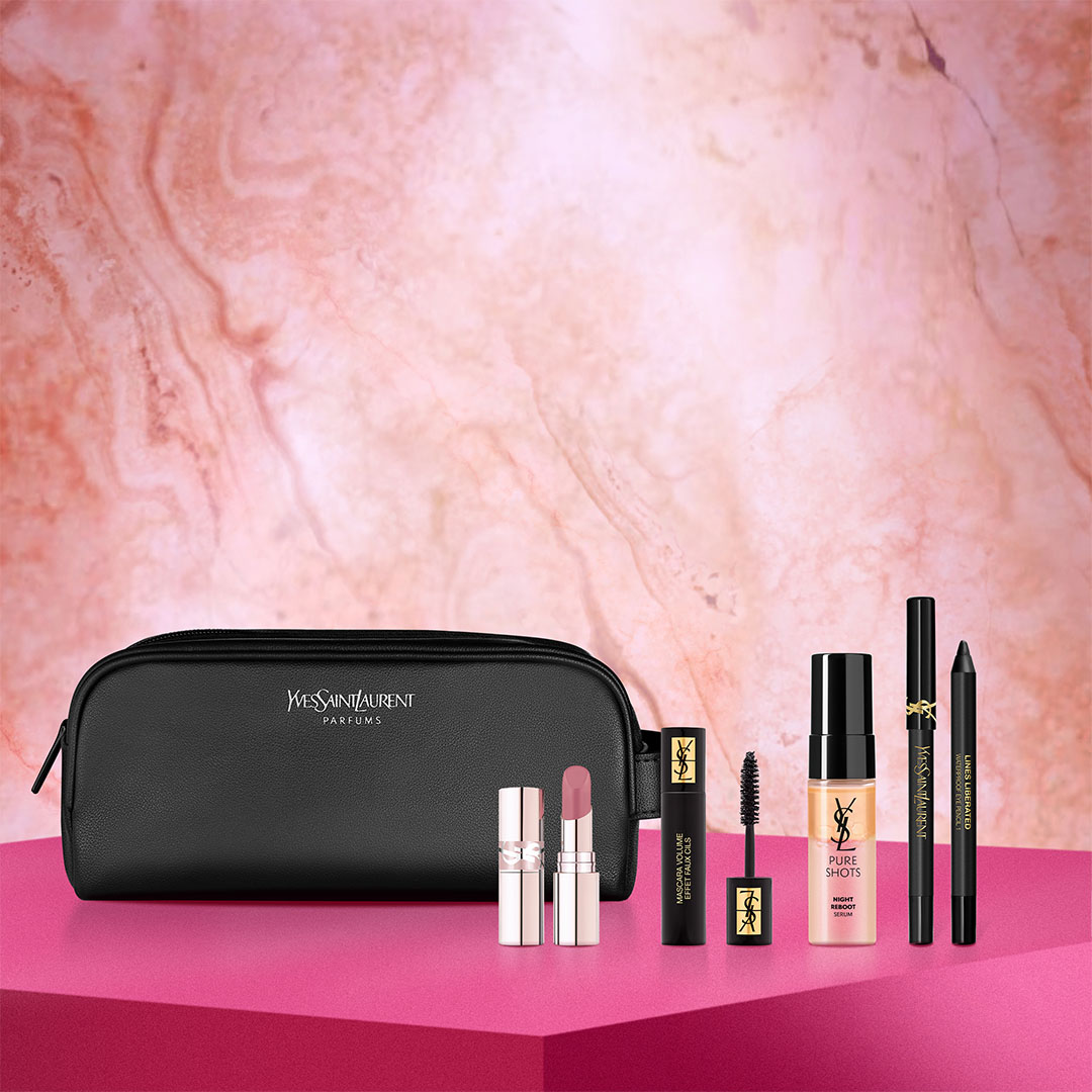 A black Yves Saint Laurent makeup bag and a collection of YSL beauty products including Pure Shots mousse, Libre perfume, mascara, and lipstick are displayed on a white marble surface, with a prominent gold YSL logo to the left.