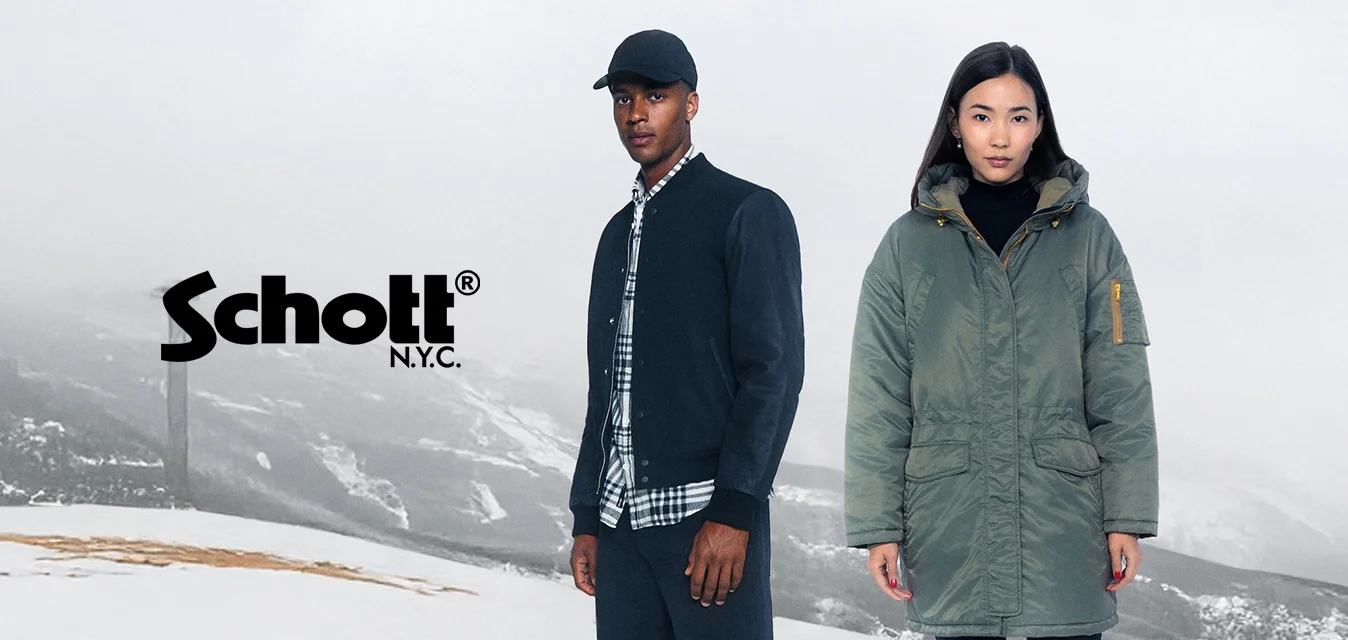 Due persone si trovano su un terreno coperto di neve. L'uomo indossa una giacca bomber scura e una camicia a quadri, mentre la donna è in una parka verde con cappuccio.