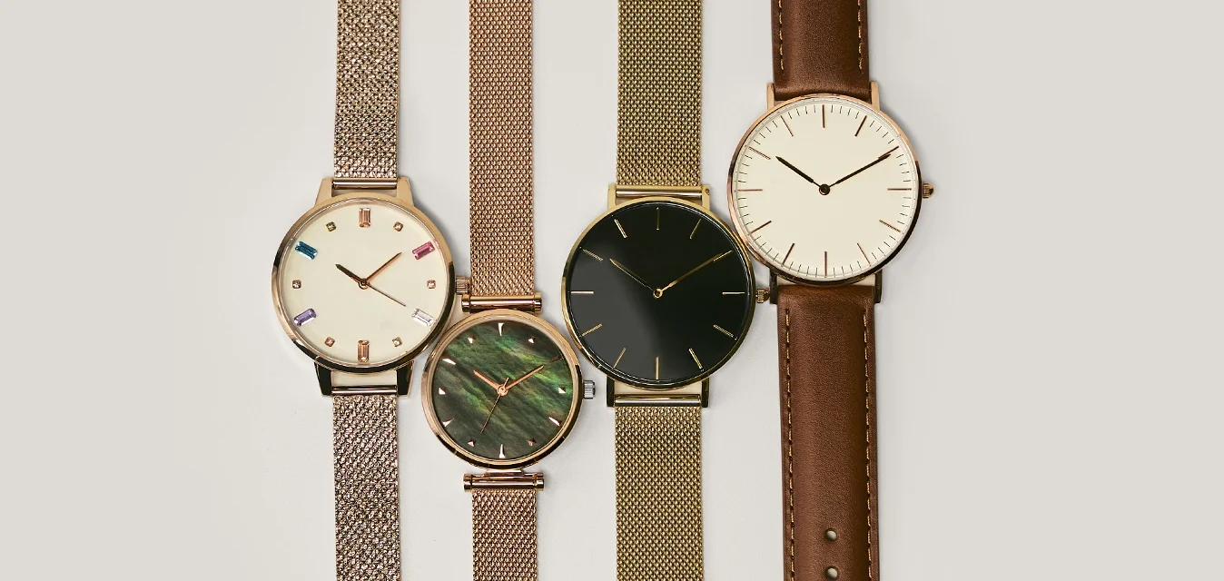 Quattro orologi analogici esposti: due con cinturini a rete metallica (color oro), uno con un quadrante in marmo verde e uno con cinturino in pelle marrone.