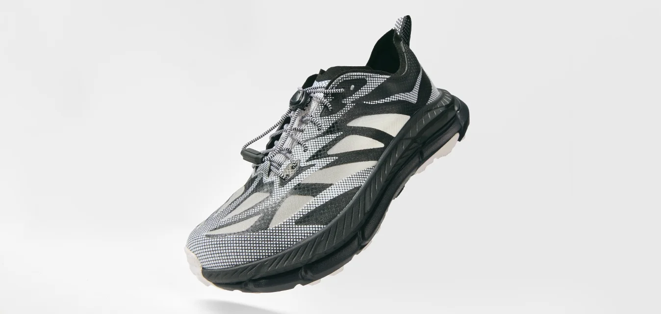 Scarpa sportiva nera e grigia con tomaia in rete pattern, lacci sicuri, suola spessa e ammortizzata, mostrata in angolo su uno sfondo bianco.