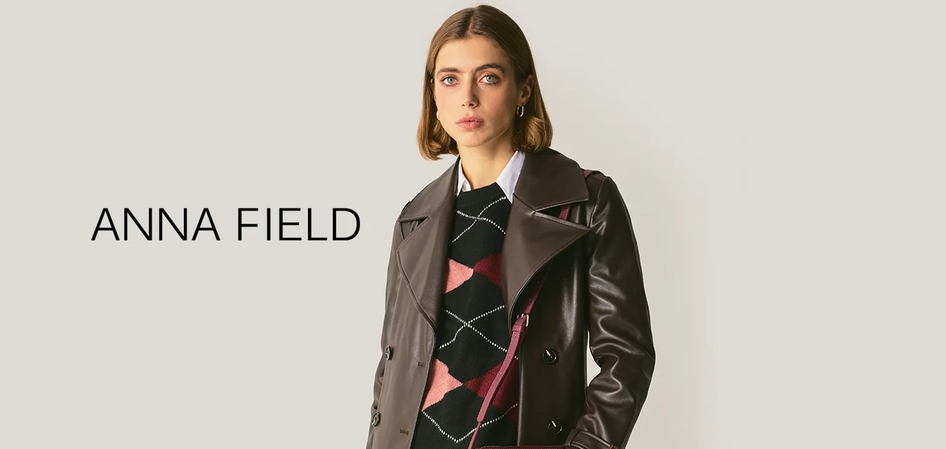 Cappotto trench in pelle marrone con ampio colletto e design doppiopetto, abbinato a un maglione nero a motivi e a una borsa in pelle di coccodrillo color amaranto.