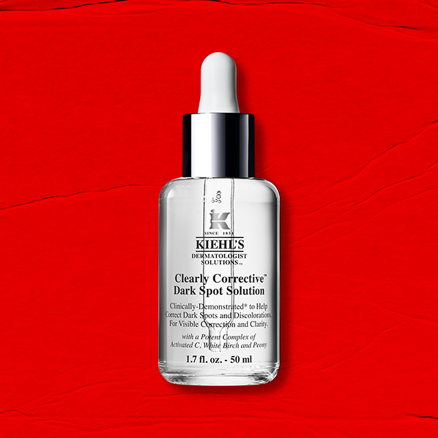 Flacone trasparente di Clearly Corrective Dark Spot Solution su sfondo rosso texturizzato.