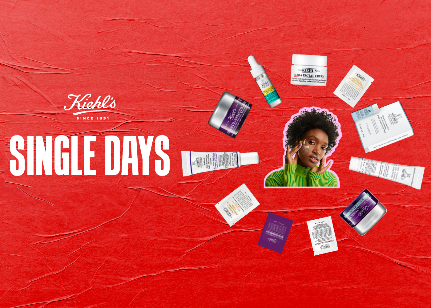 Visual Kiehl’s Single Days con sfondo rosso testurizzato. Al centro una persona con maglione verde applica crema viso, circondata da prodotti skincare Kiehl’s e campioni disposti in cerchio attorno al testo “Single Days”.